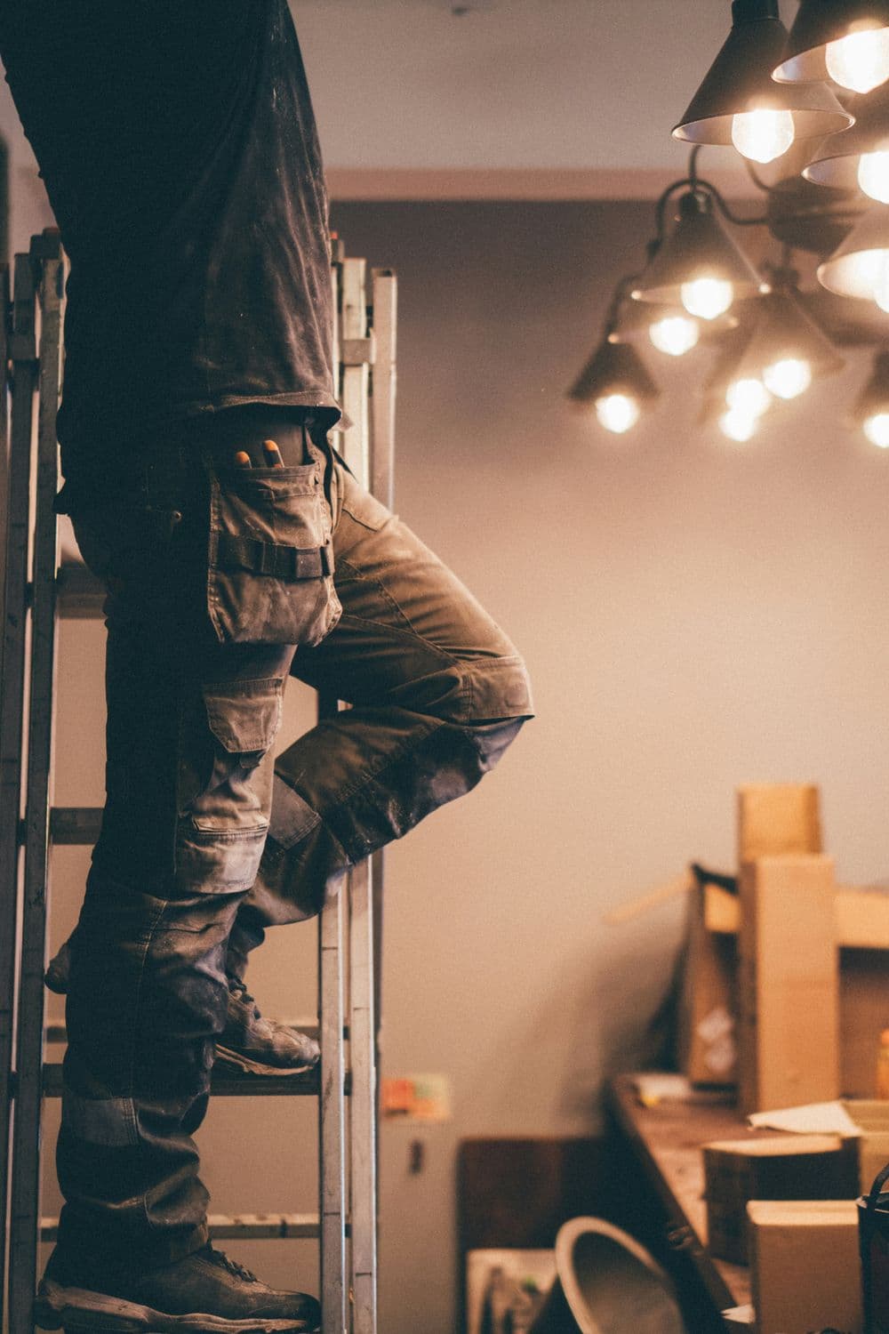 Worker on a ladder adjusting lights in a construction workspace.